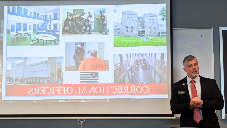 a corrections director speaks to a class of students in front of a powerpoint